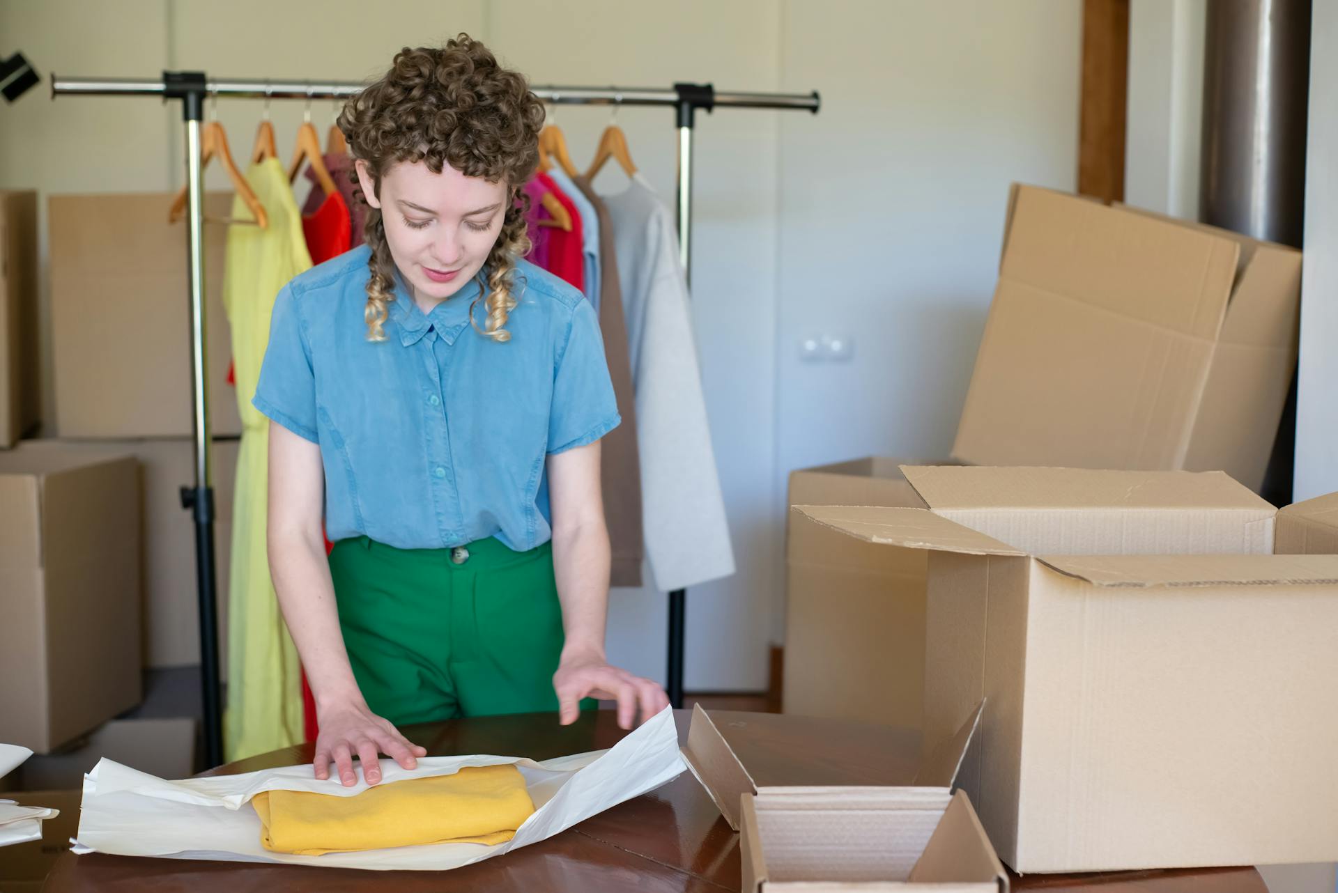 A young female entrepreneur packaging clothes in eco-friendly boxes in her online store workspace.