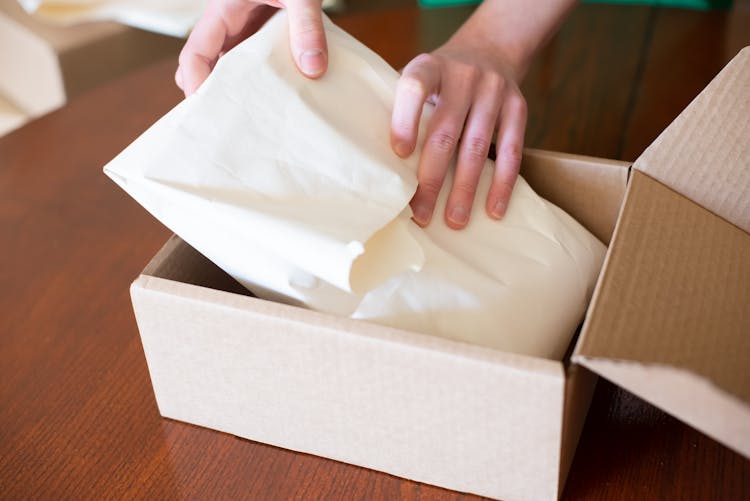 Close-up Of Person Packing An Order Into A Cardboard Box