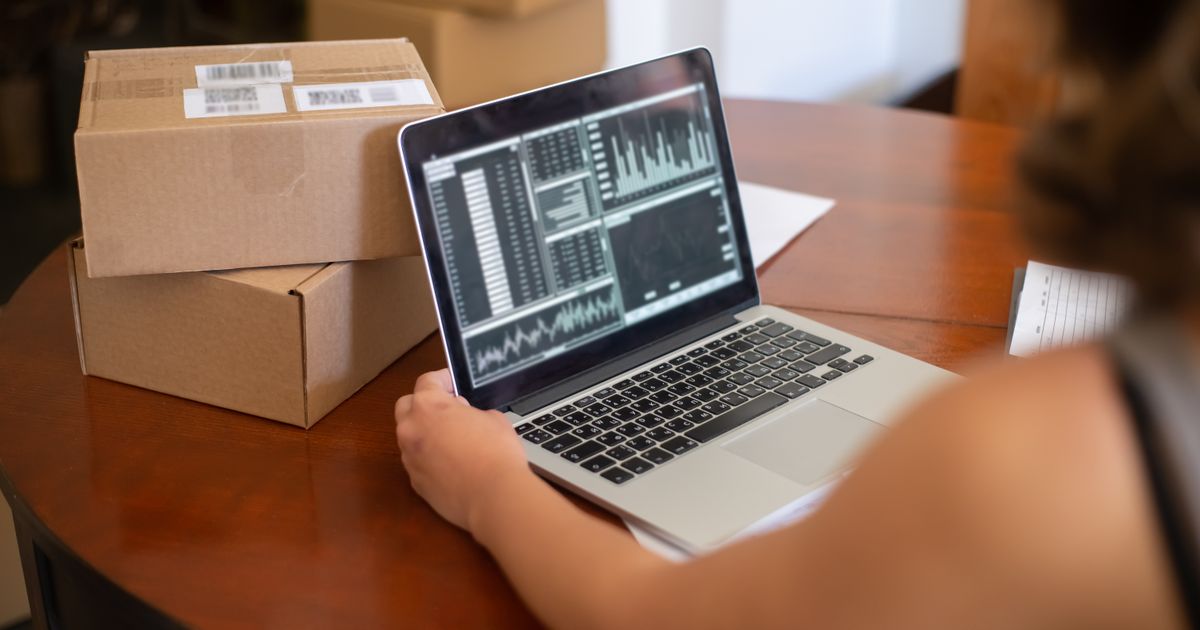 Une personne consulte les statistiques de sa boutique en ligne sur un ordinateur portable, deux colis prêts à partir posés à côté.