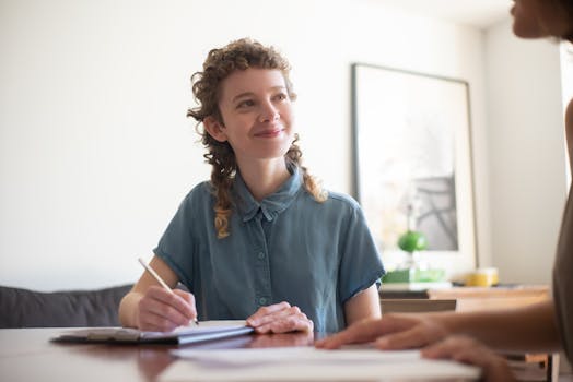 Young woman smiling and writing with a pen at a table indoors.