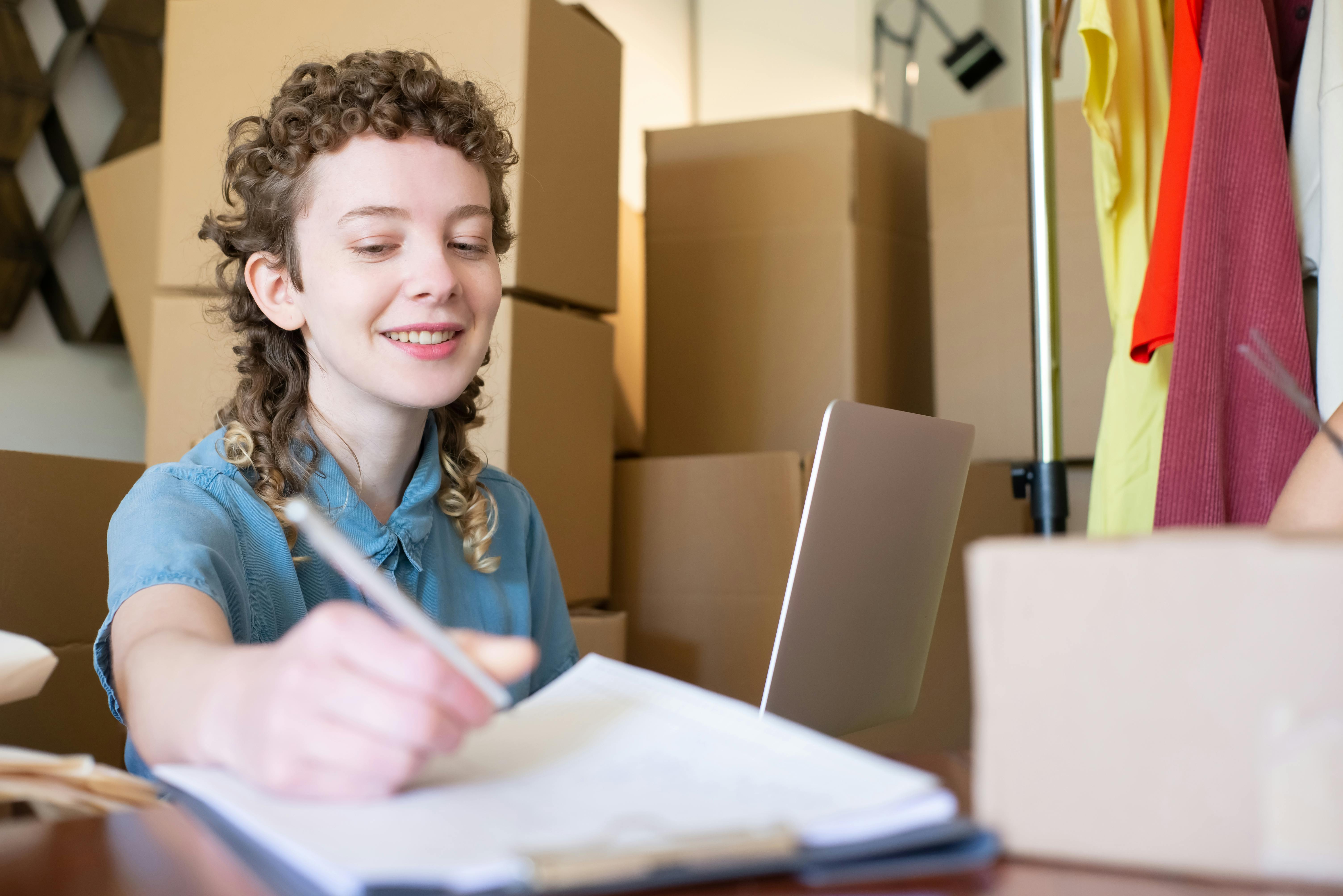 Smiling young woman managing a small business with laptop and packages around her.