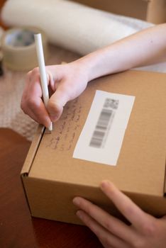 A hand writing on a brown shipping box label, capturing a personal touch in packaging.