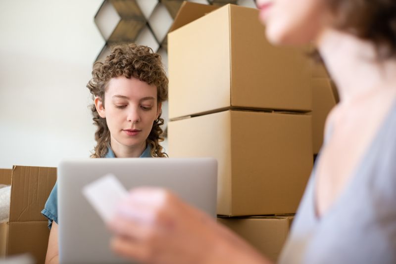 Woman managing a small online business surrounded by cardboard boxes and a laptop while fulfilling orders