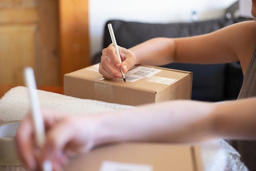 Free Person Writing on Brown Cardboard Box Stock Photo
