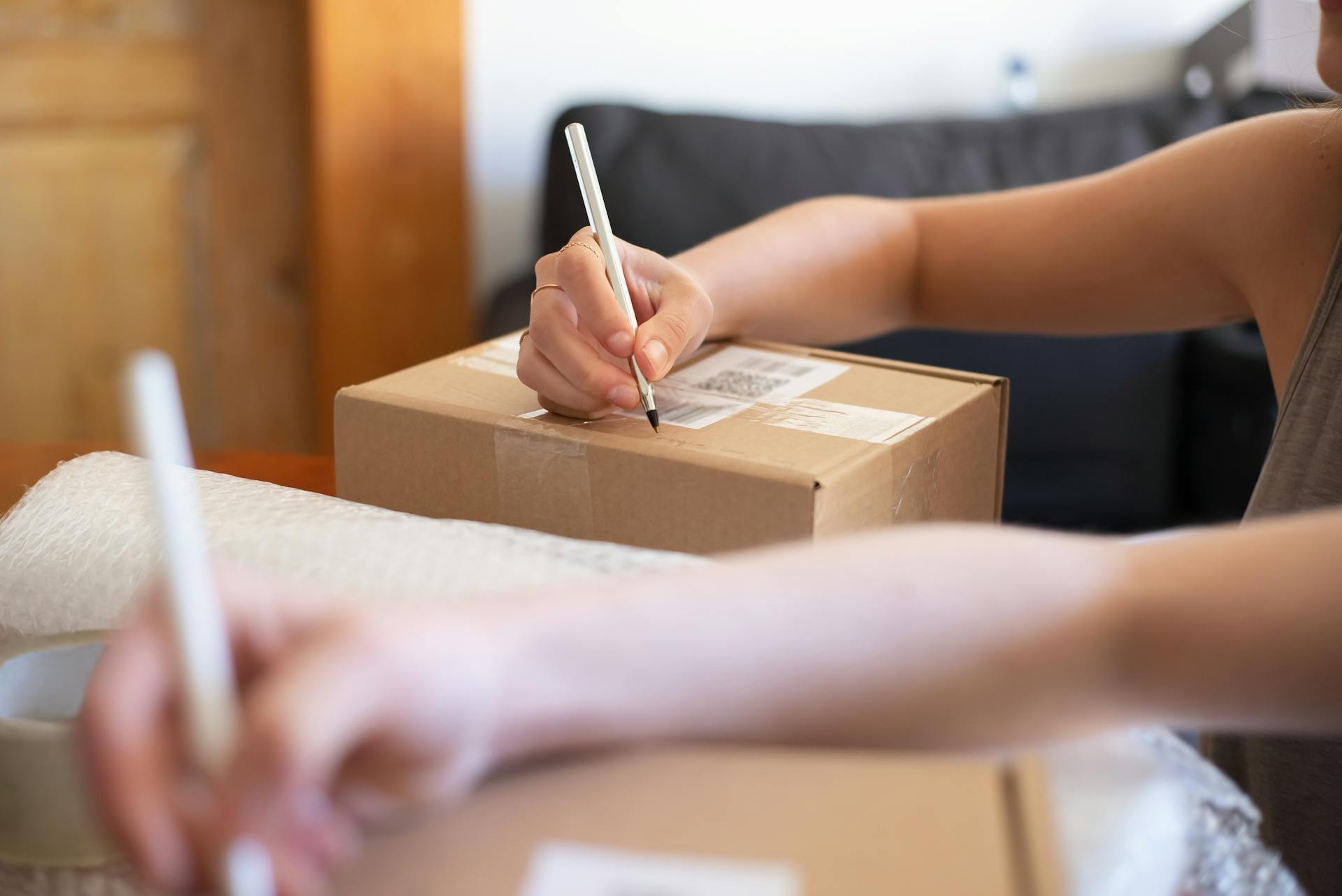 Close-up of hands labeling a cardboard box for online shipping from a home office.