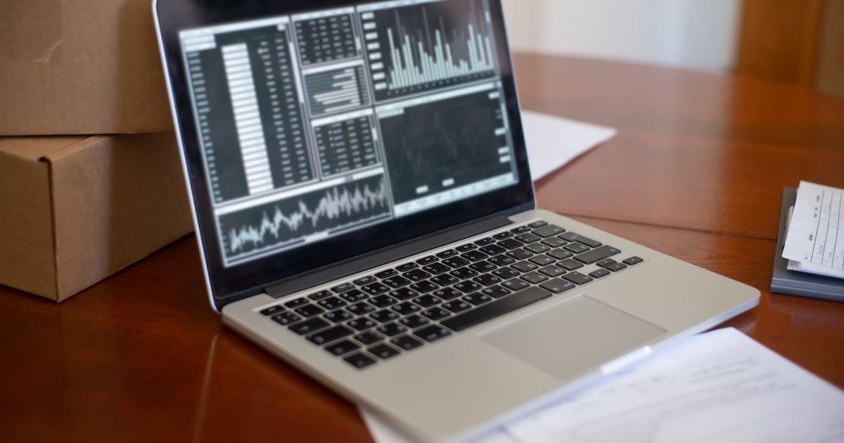 Laptop showing data graphs on a wooden table beside cardboard boxes in a small business office