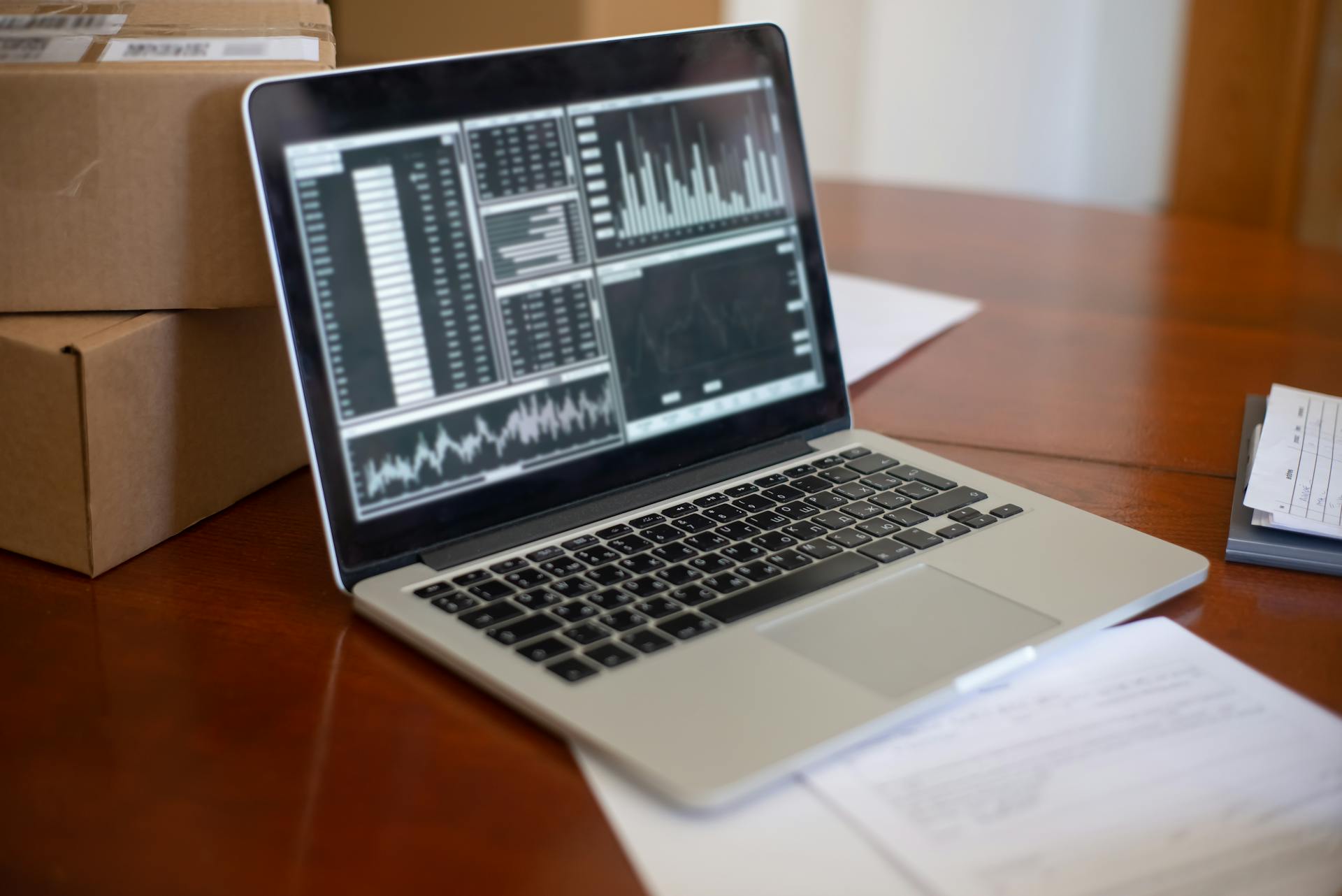 Laptop showing data graphs on wooden table with cardboard boxes, depicting a small business office setting.