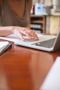 Close-up of a woman using a laptop at a wooden desk, focusing on hand engagement.