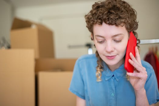 Smiling young woman talking on her phone surrounded by moving boxes indoors.
