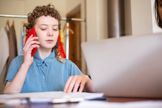 A woman with curly hair talks on the phone while working at a desk, highlighting a remote work lifestyle.