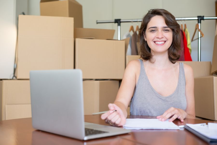 Happy woman working on a laptop surrounded by cardboard boxes. Ideal for business and online store concepts.