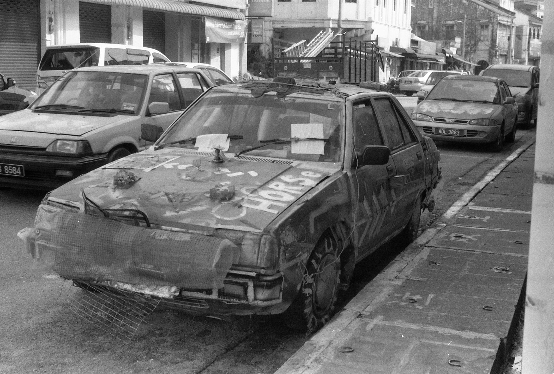 Grayscale image of vandalized cars on an empty street conveying urban decay.