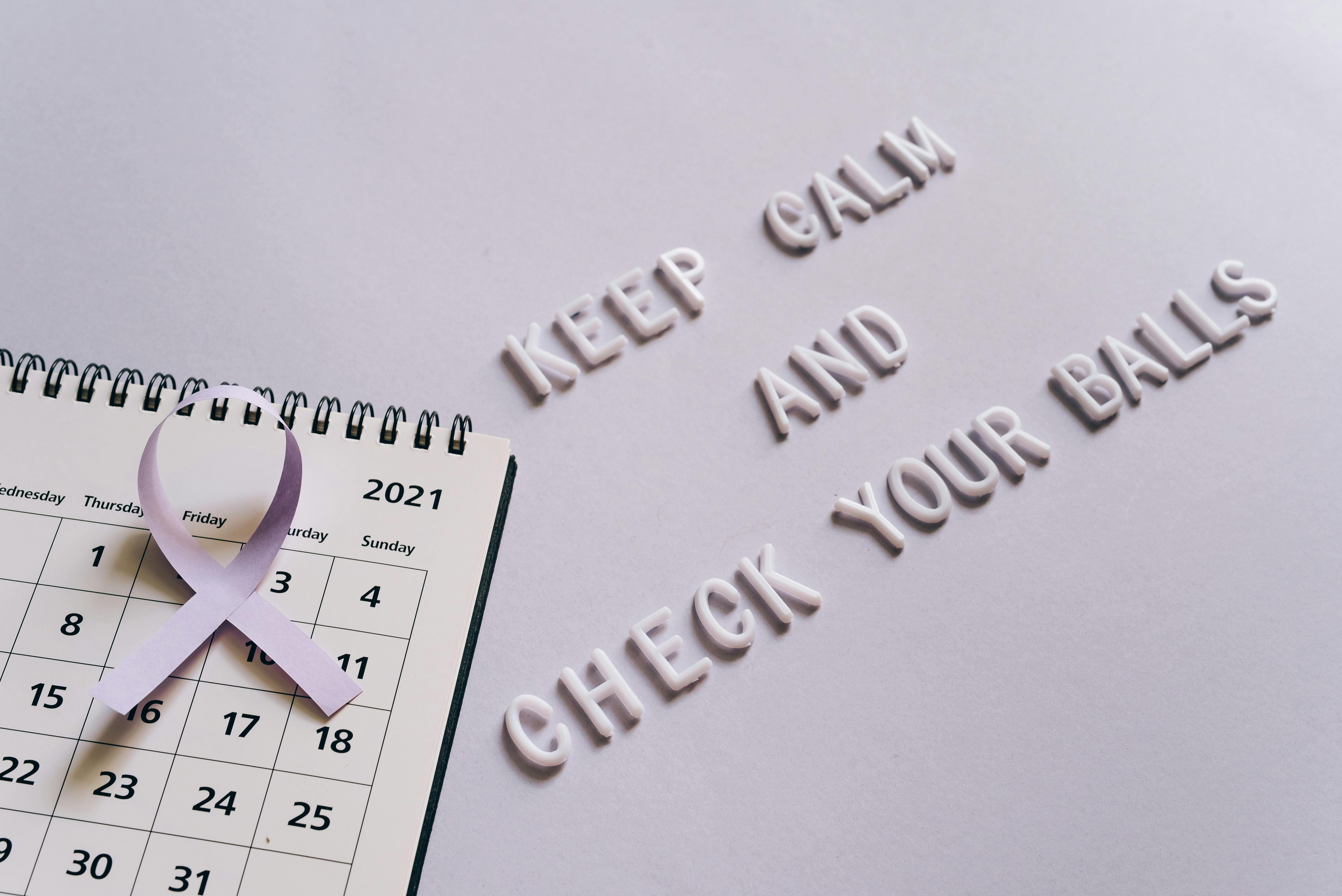 Flat lay image of a calendar with a purple ribbon and the text 'Keep Calm and Check Your Balls' for testicular cancer awareness.