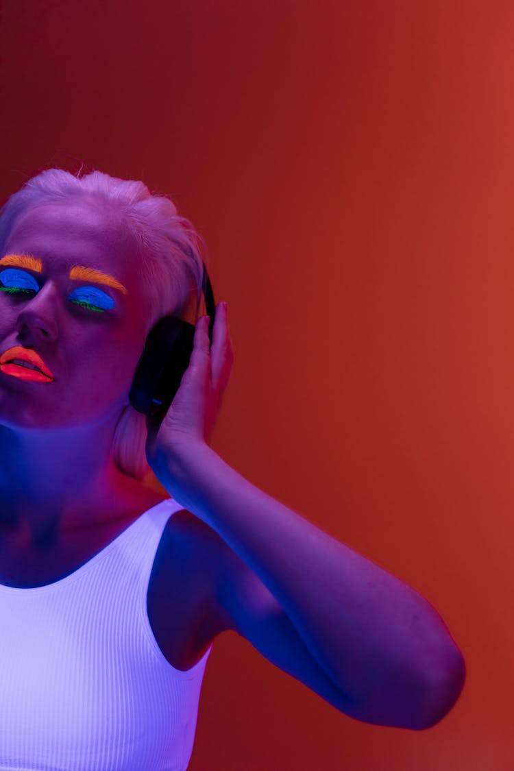 Studio Shot Of A Woman With Fluorescent Makeup Listening To Music On Headphones In UV Lighting 