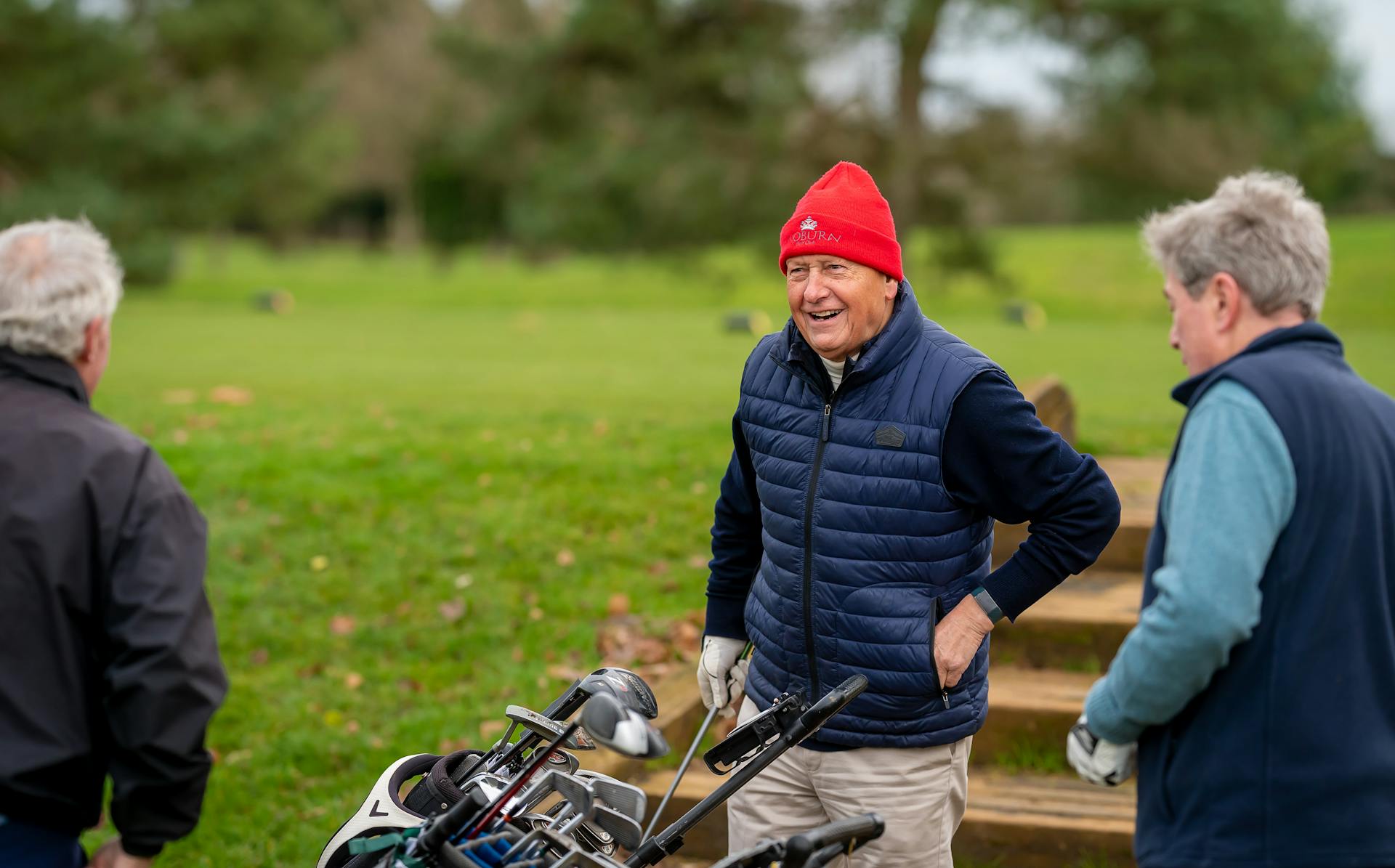 Three senior men enjoying a round of golf on a sunny day, interacting happily.