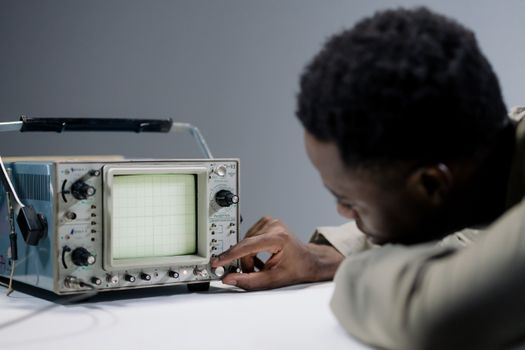 A person operates a vintage oscilloscope, adjusting controls in a studio setting.