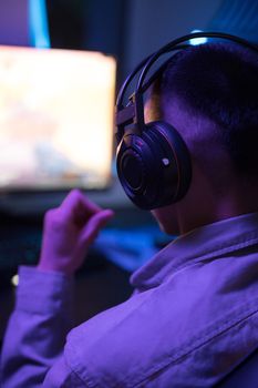 A young man wearing headphones, focused on a video game screen in a dimly lit room.