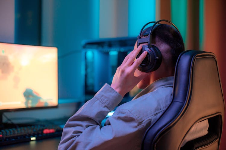 Man Holding His Headphones While Playing On A Computer 