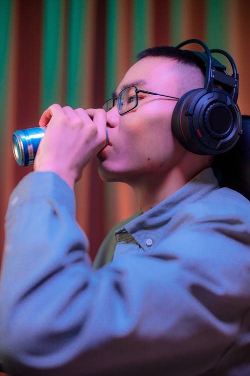 A Man Wearing Headphones Drinking a Canned Beverage