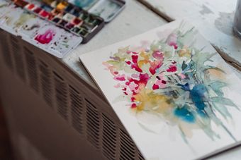 Loose floral watercolour painting drying on a sketchpad beside a paint palette — photo by Greta Hoffman on Pexels