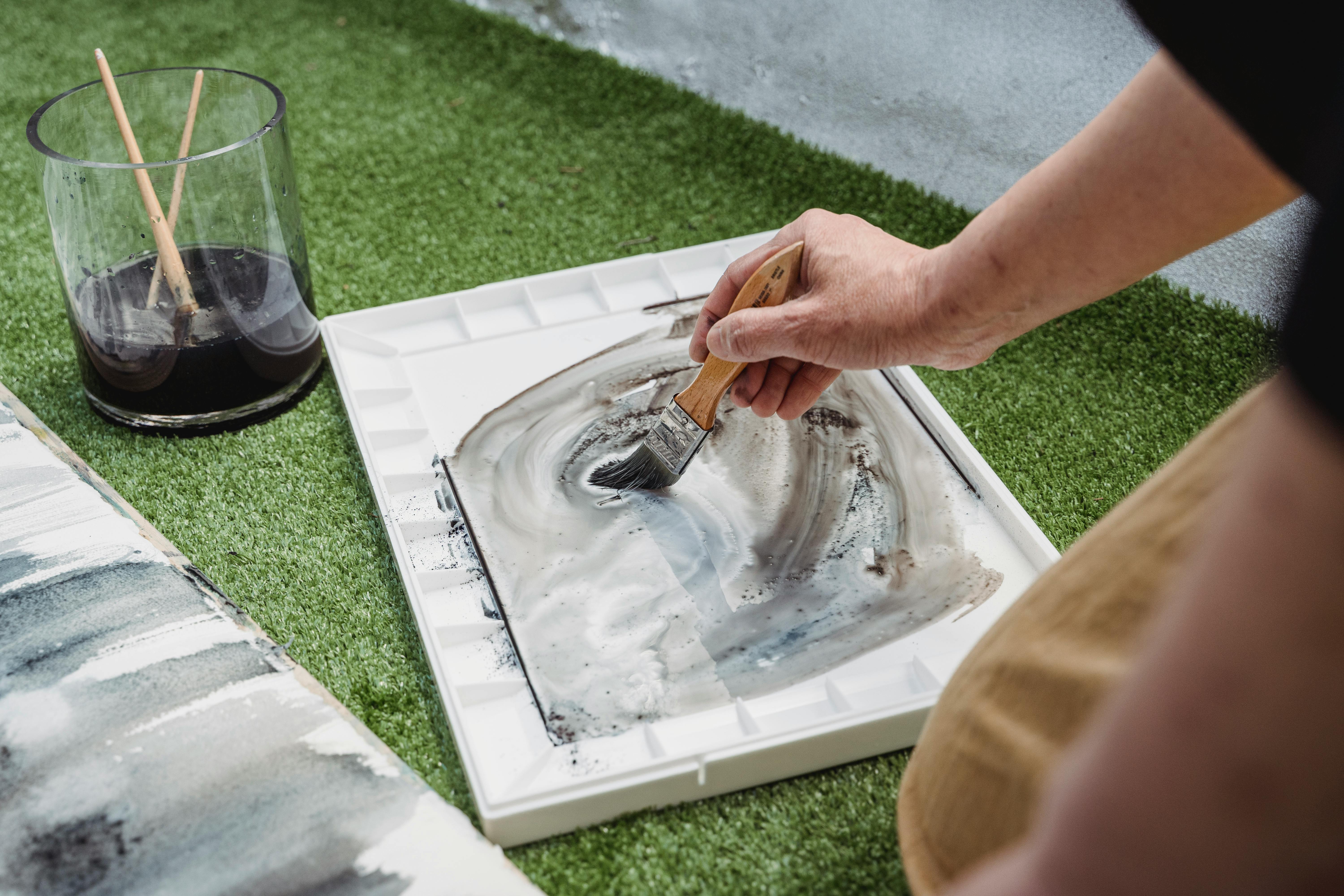 Close-up of an artist mixing paints on a palette outdoors, emphasizing creativity and handcraft skills.