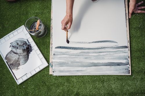 Free A person creates abstract art outdoors using brushstrokes on canvas. Creative expression on grass. Stock Photo
