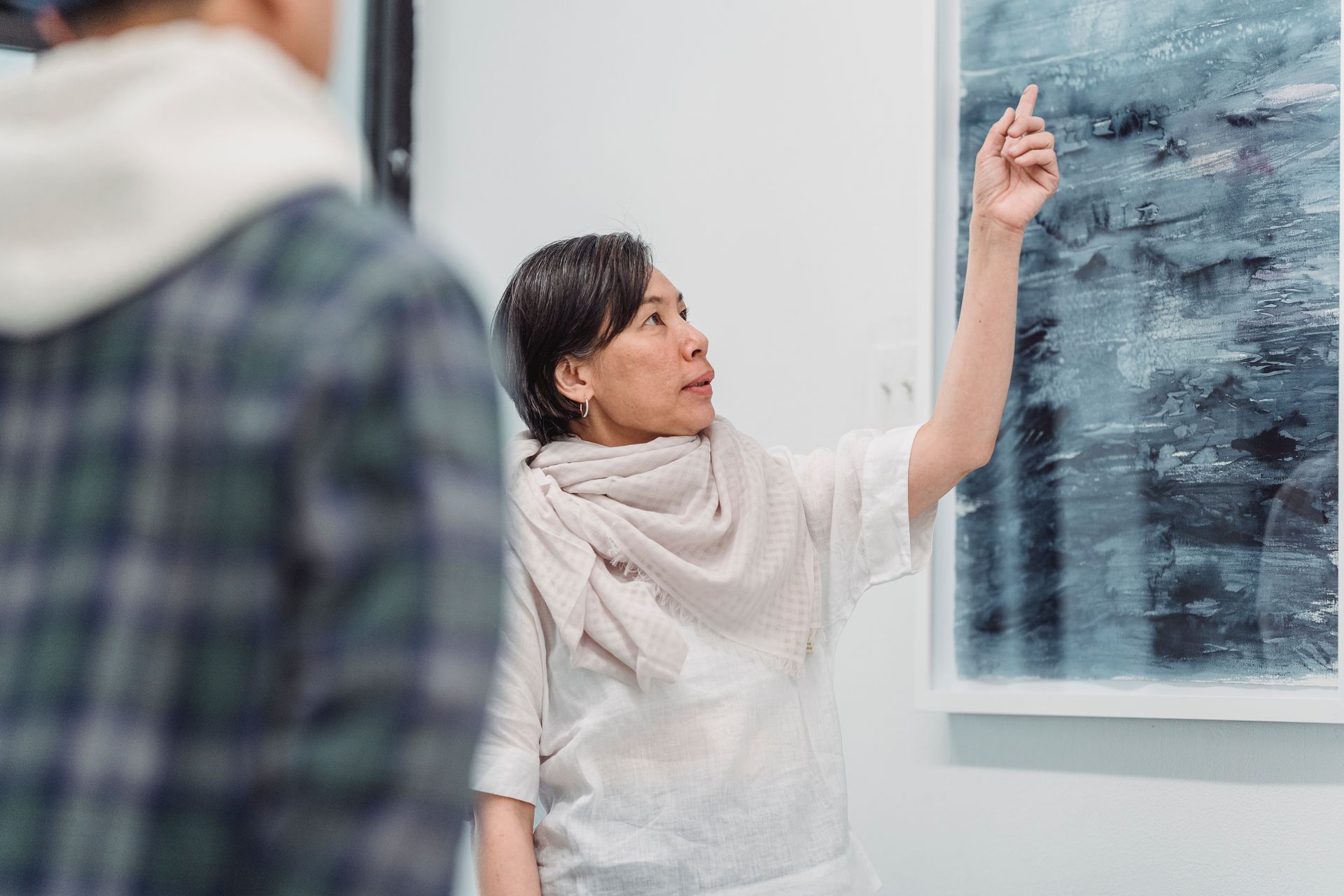 Woman presenting abstract painting in an art gallery setting, engaging discussion.
