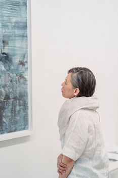 A woman in an art gallery closely observes an abstract painting, captivated by its details.
