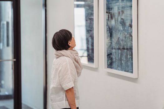 A woman in a gallery intently observes abstract paintings, highlighting her engagement with modern art.