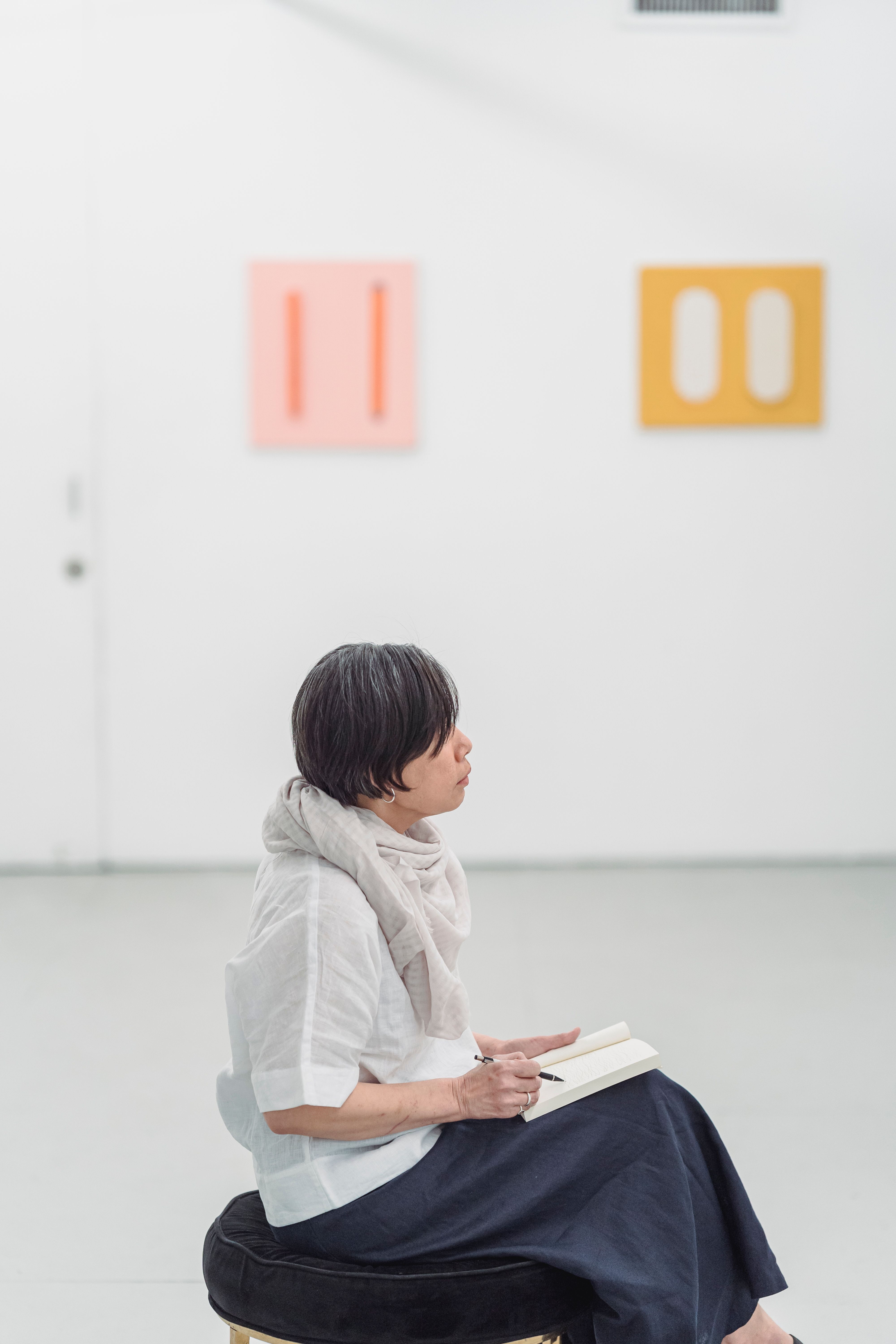A woman seated in a gallery, immersed in thought with a sketchpad.