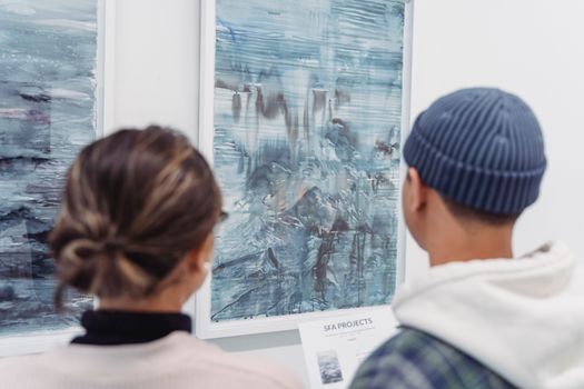 Visitors admire abstract paintings in an art gallery, showcasing modern artistic expressions.