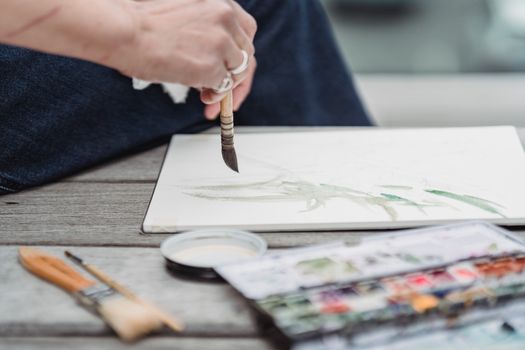 Close-up of an artist using watercolor paints on a sketchpad outdoors, emphasizing creativity.