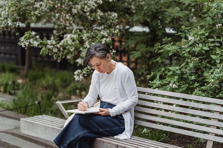 Woman Sitting On A Bench While Drawing In A Sketchpad