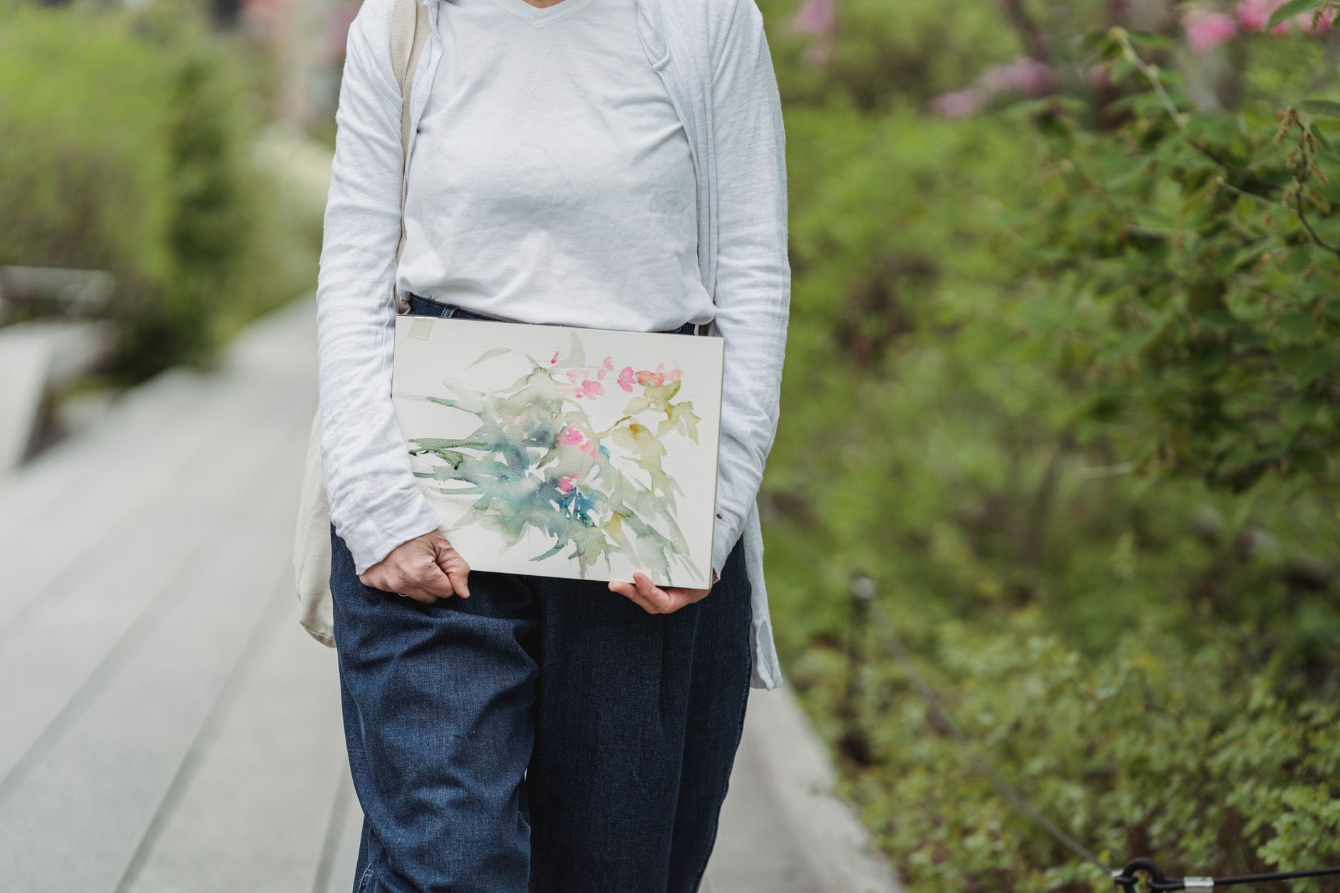 A woman carrying a watercolor painting while walking outdoors, showcasing artistic creativity.