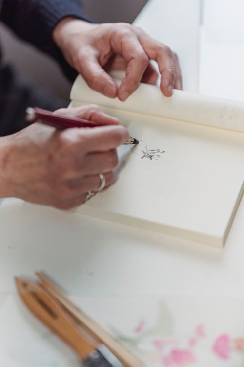 Free Close-up of hands drawing with a pen in a sketchbook, illustrating creativity and artistic expression. Stock Photo