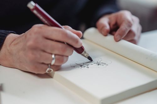 Free Artistic close-up of hands sketching flowers on paper with a pencil. Stock Photo