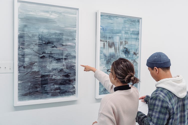 Man And Woman Standing Near The Abstract Paintings Hanged On The Wall