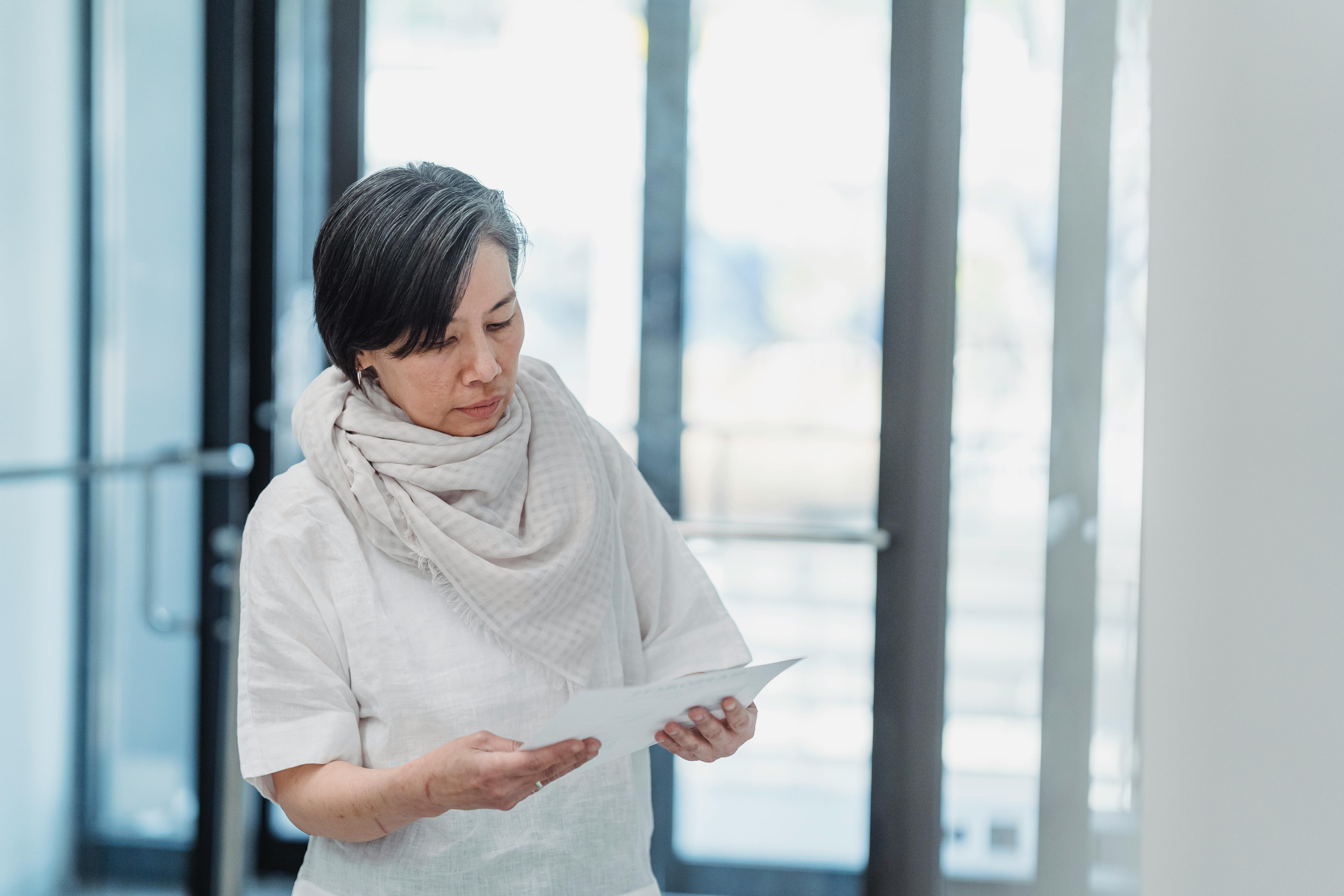 A senior woman reading papers in a bright office setting, exhibiting focus and concentration.