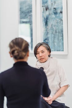 Two women engaged in a professional interview indoors with artwork in the background.