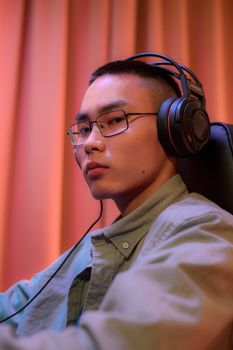Young man wearing eyeglasses and headphones in moody ambient lighting.