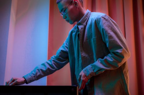 Free Side view of an Asian man adjusting equipment indoors under colorful lighting. Stock Photo