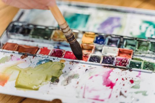Colorful watercolor palette in use with a paintbrush applying paint, showcasing messy artistic creativity.