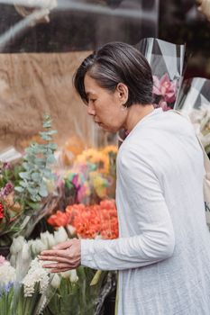 A woman in a white outfit explores vibrant flowers at an outdoor market, capturing spring vibes.