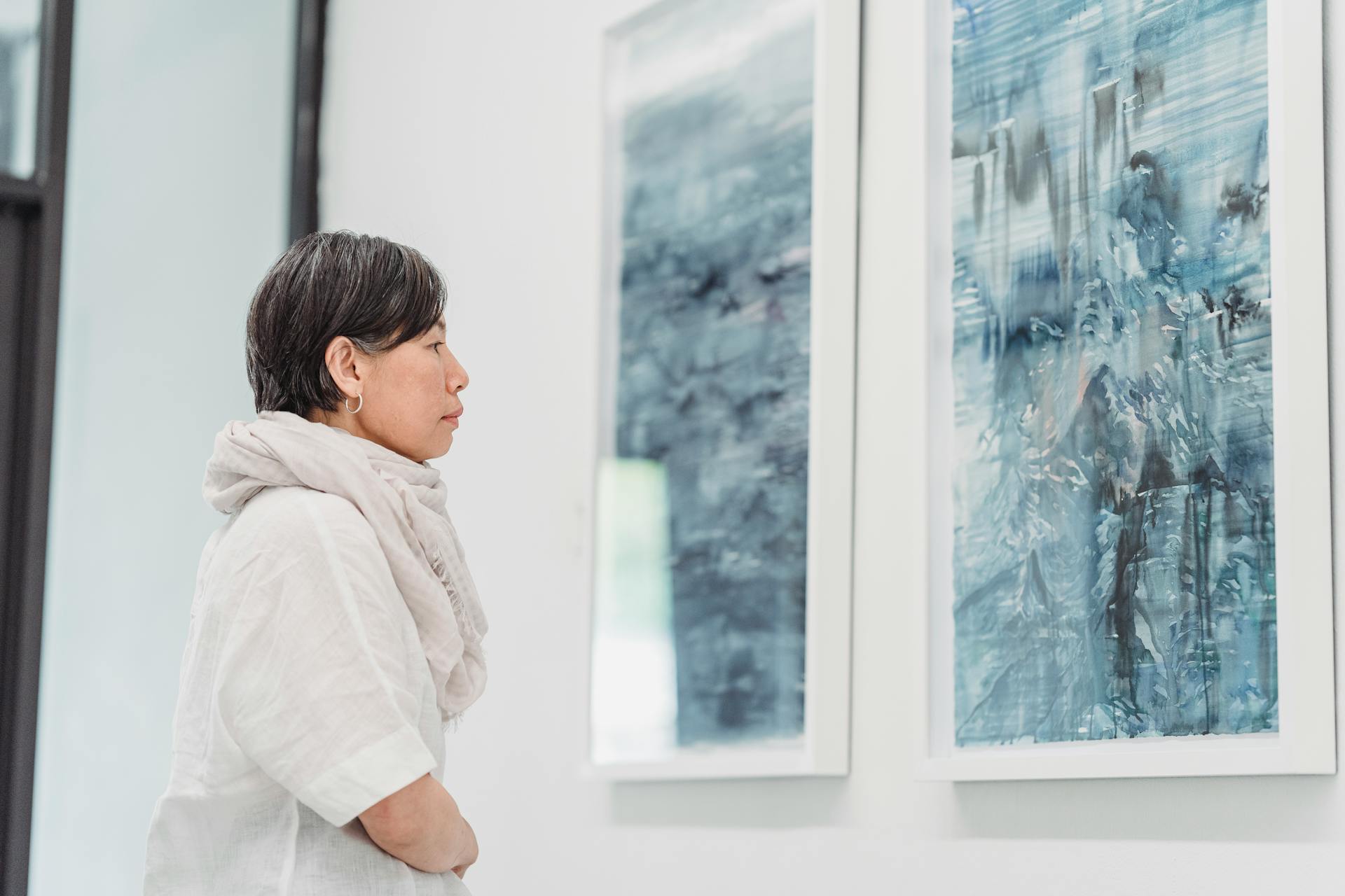 Woman gazing thoughtfully at abstract paintings in a modern art gallery exhibit.