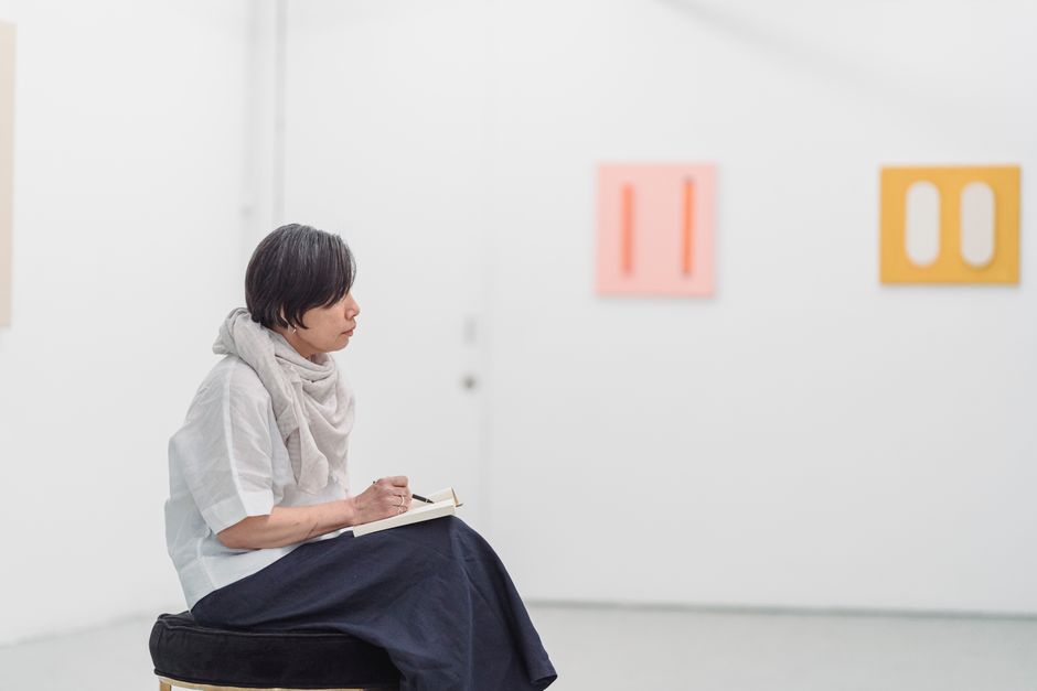 女性が現代美術館で思慮深くスケッチをし、ミニマリストのアートに囲まれています。