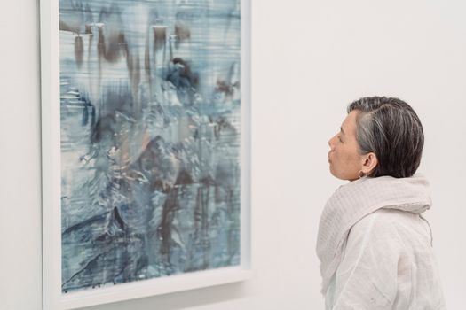 A woman observes an abstract painting in a gallery, reflecting art appreciation.