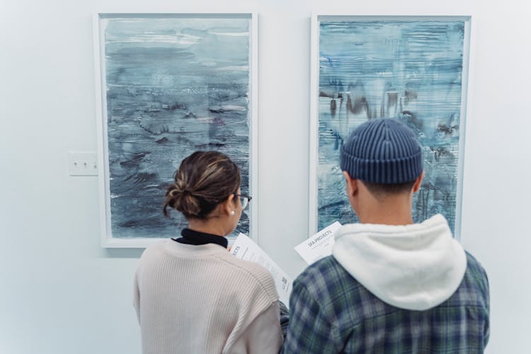 Back View Of Man And Woman Standing Near The Abstract Paintings Hanged On The Wall