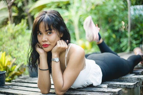 A Woman in White Tank Top and Black Leggings Lying Down with Her Hands on Her Chin