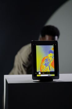 A tablet displaying an infrared image with a person partially visible in the background.