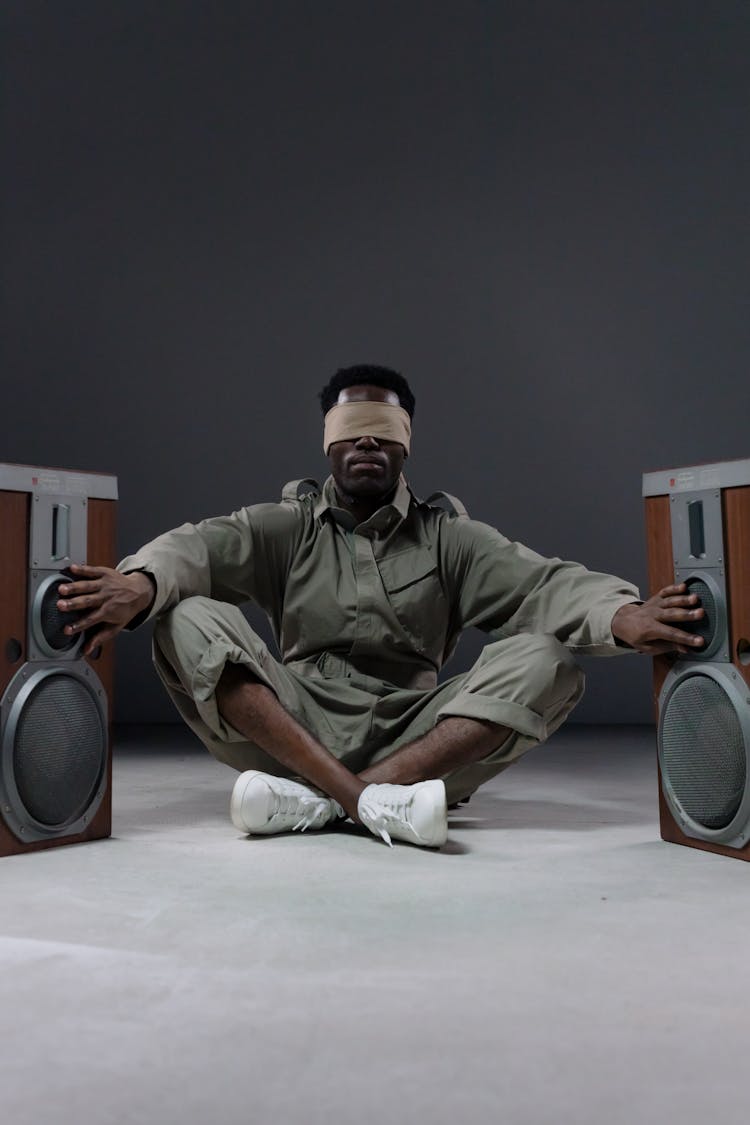 Blindfolded Man Sitting Between Speakers